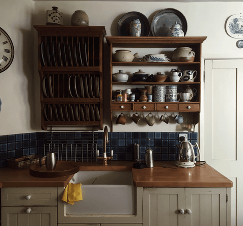 Handmade mugs and dishware displayed on a wooden kitchen shelf